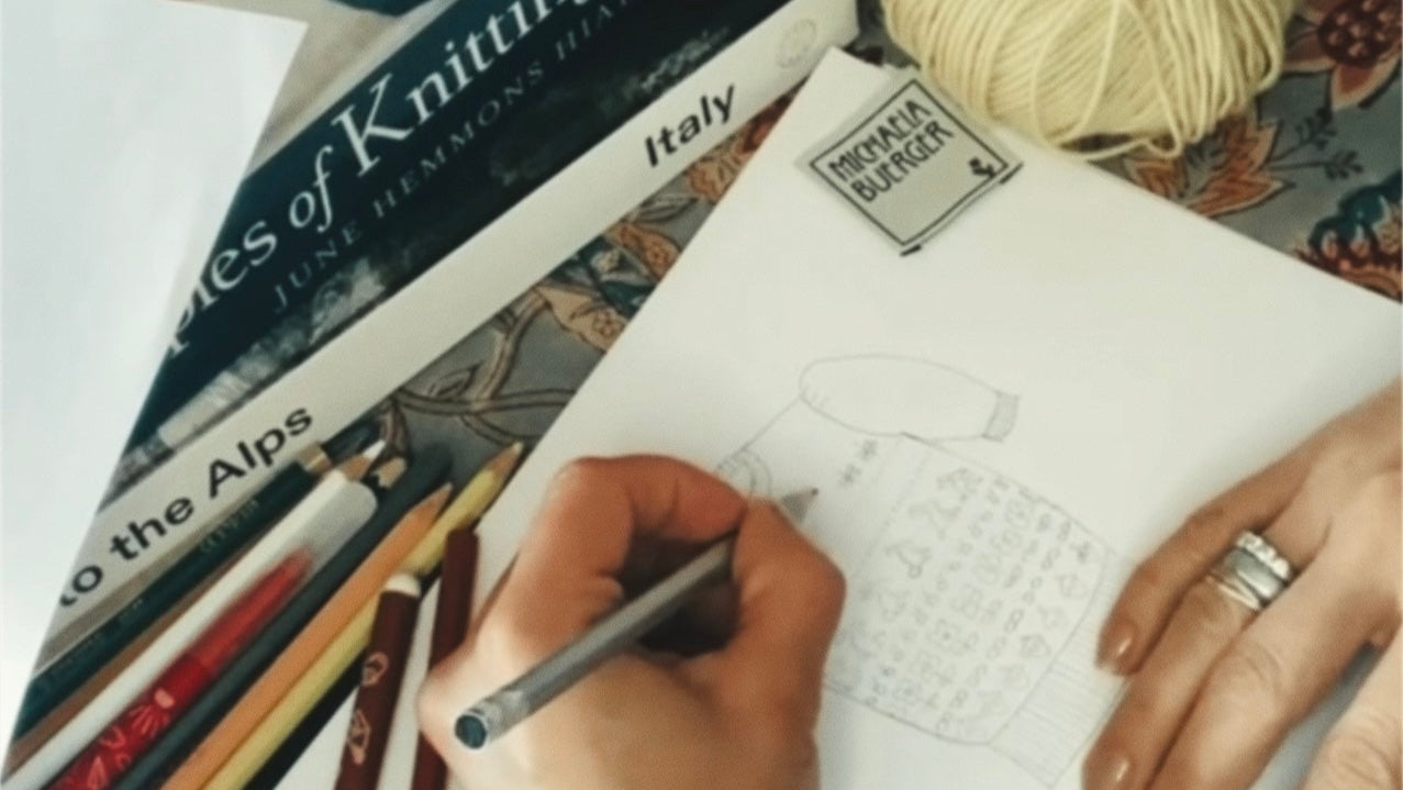 Person knitting with yarn and knitting needles, surrounded by books and patterns.