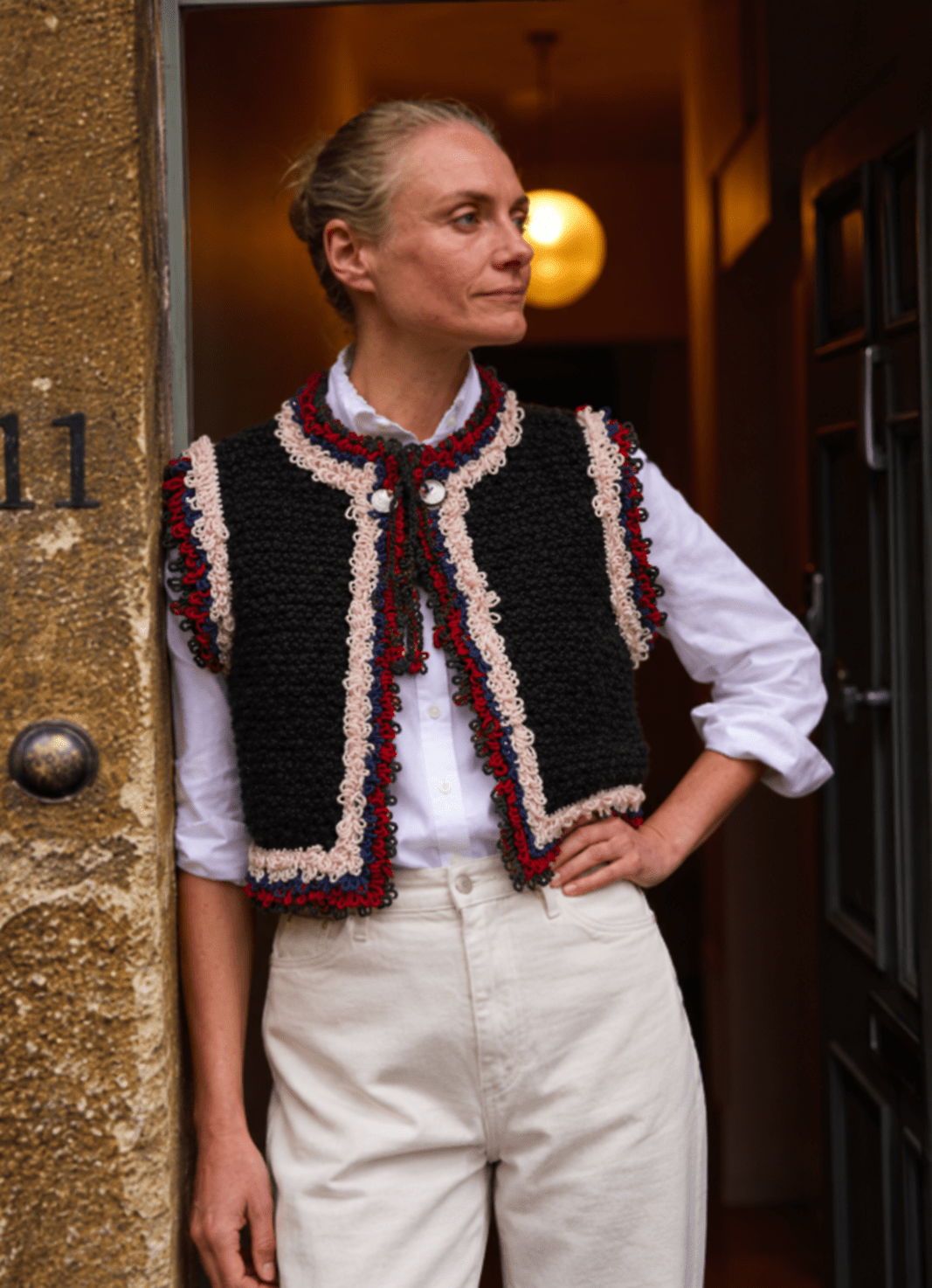 Mountain Vest in Black, a hand-knitted Alpine-inspired wool vest with multicolor crochet fringe, worn over a white shirt.