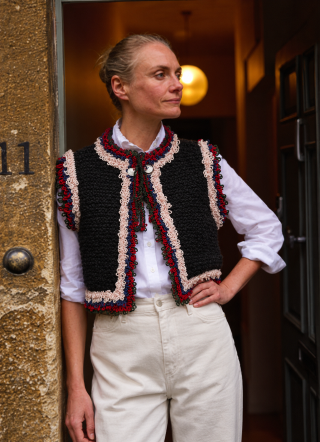 Mountain Vest in Black, a hand-knitted Alpine-inspired wool vest with multicolor crochet fringe, worn over a white shirt.