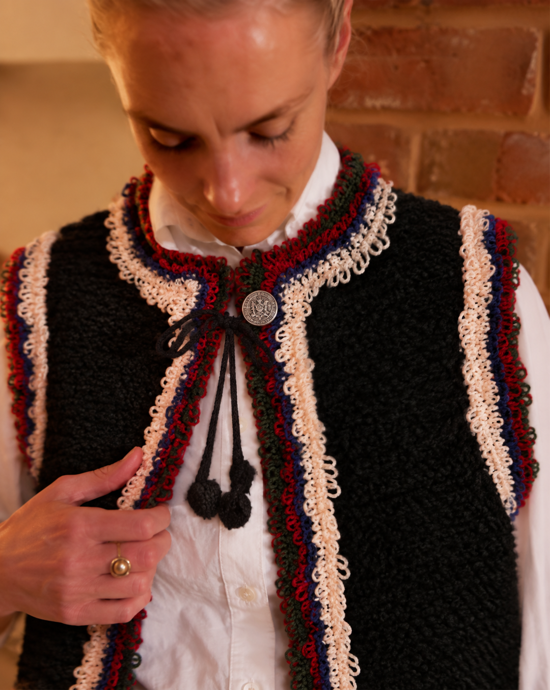 Detail of the Mountain Vest in Black, a hand-knitted wool vest with multicolor crochet fringe and decorative silver coin button.