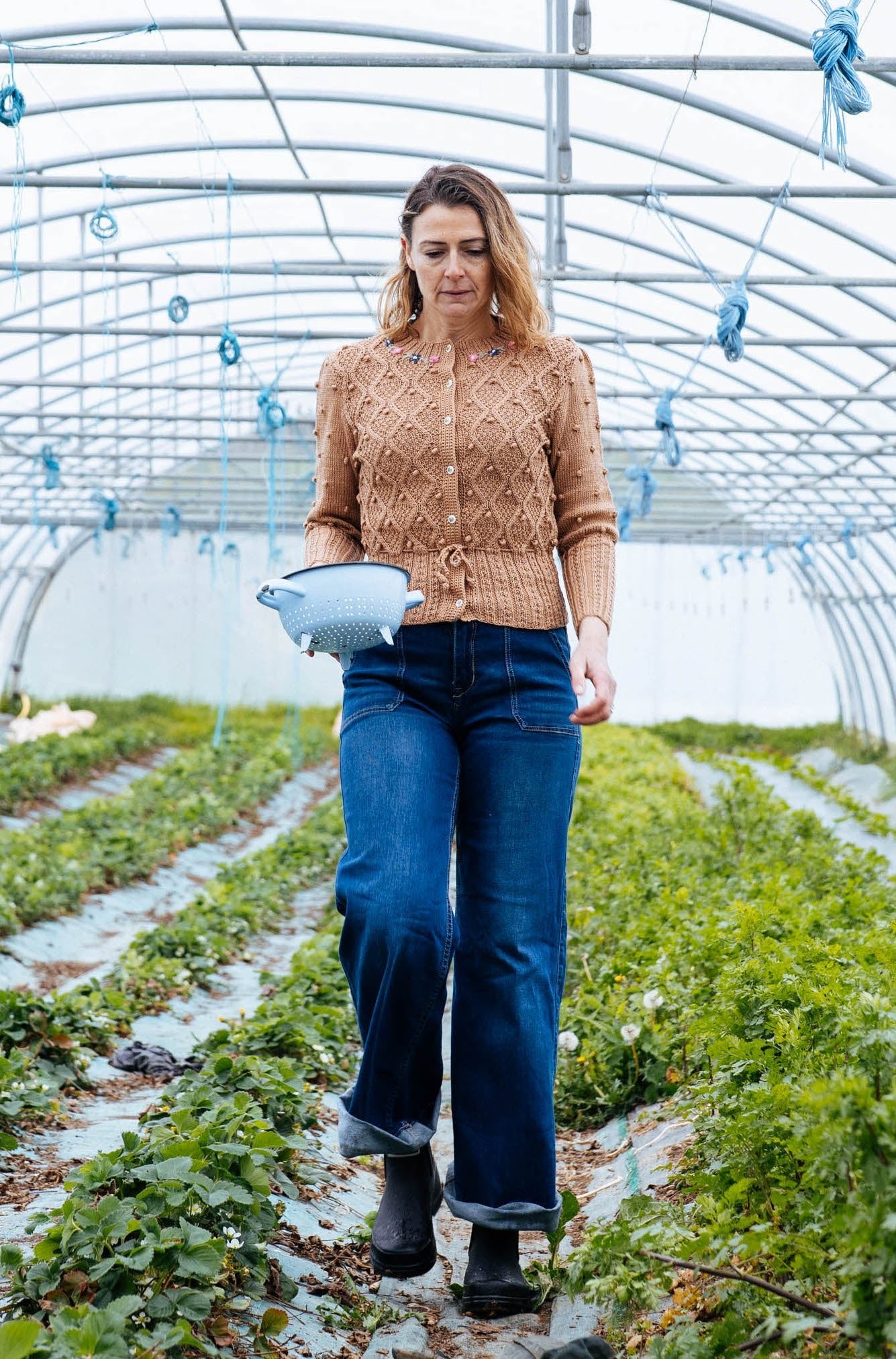 Woman wearing alpine clay cotton hand knitted cardigan walking in greenhouse